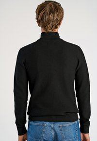 Maglione nero lavorato a maglia con colletto alto, tessuto testurizzato, polsini e orlo affusolati, mostrato da dietro su uno sfondo neutro.