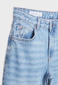 Svetlomodré džínsové nohavice s vysokým pásom, s prednou vreckom, mosadznými nitmi a vyblednutou textúrou. Na štítku je napísané "Stradivarius."