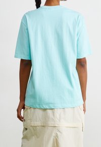 Ljusblå t-shirt i bomull med kort ärm och rundad hals, visad från baksidan. Lätt oversized passform, minimal design.