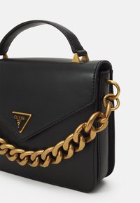 Černá kožená kabelka se zlatým řetězovým popruhem přes rameno, trojúhelníkovou logovou destičkou a hranatými zlatými prvky na vrchu. Kompaktní obdélníkový tvar.