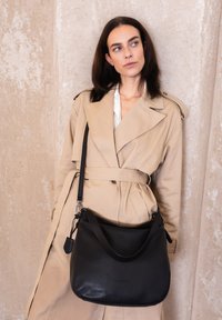 Borsa a spalla in pelle nera con design morbido, texture liscia e una sola tracolla. Presentata su uno sfondo neutro.