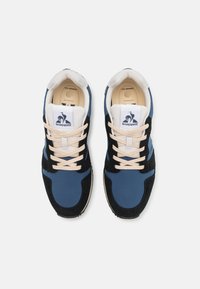 Zapatillas azul y negras con parte superior de ante y tela, cordones beige, logo en la lengua y plantilla acolchada. Diseño de puntera redonda, adecuadas para un uso casual.