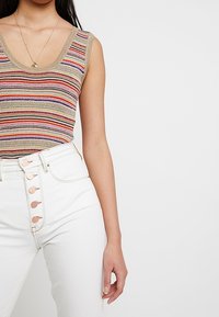 Randig stickad linne med V-hals, i färgerna beige, röd och lila; kombinerad med höga vita jeans med knäppning.