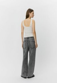 Top in cotone bianco a coste con scollatura a oblò, abbinato a jeans grigi in denim a vita alta e dal taglio morbido con due tasche posteriori.