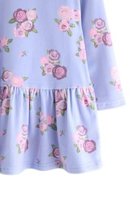 Jasnofioletowa sukienka z różowymi i fioletowymi wzorami róż oraz falbaną na dole spódnicy.