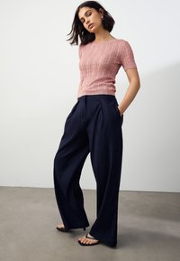 Pink ribstrikket kortærmet top kombineret med vidbenede marineblå bukser. Bukserne har lommer og plisseret design. Glat tekstur.