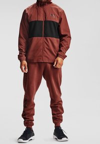 Chándal deportivo para hombre en burdeos y negro, con chaqueta de cremallera y diseño a bloques de color, y pantalones entallados a juego. Textura suave.