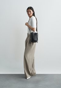 Μαύρη πλεκτή τσάντα ώμου με κλείσιμο ροπάλου, συνδυασμένη με λευκό ριμπ μπλουζάκι και μπεζ παντελόνι ψηλόμεσο, φαρδύ.