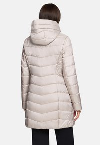 Manteau matelassé beige clair avec capuche, arborant un motif chevron, manches longues, et une longueur mi-cuisse. Tissu lisse et brillant.