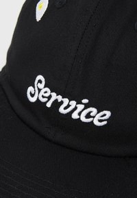 Black cap featuring white embroidered text “Service” and a small yellow and white design on the front. Classic curved brim and textured fabric.