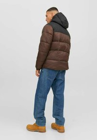 Pruun sulejope musta kapuutsiga, millel on kattereie õmblused ja elastsed mansetid, kombineeritud siniste teksade ja kollaste saappastega.