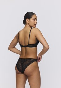 Black lace lingerie set featuring a bralette with adjustable straps and matching panties with floral patterns and scalloped edges.