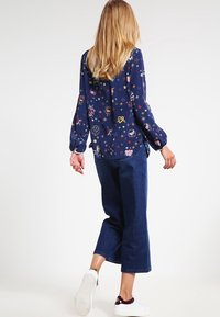 Blusa navy con motivi floreali, maniche lunghe e polsini con bottoni. Abbinata a pantaloni in denim scuri a gamba larga e sneakers bianche.