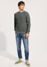 Pull côtelé vert foncé à col rond, associé à un jean droit bleu clair et des baskets vertes avec des accents crème.