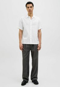 Camicia bianca a maniche corte con bottoni in tessuto testurizzato, abbinata a pantaloni grigi scuri a vita alta e scarpe nere. Design pulito e minimalista.