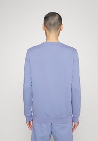 Felpa di un leggero colore viola con maniche lunghe e polsini e orlo a costine. Tessuto morbido e testurizzato, con scollatura rotonda e design minimalista.