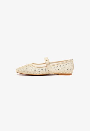 Cream-colored flat Mary Jane shoe with ankle strap and buckle, decorated with small silver studs all over.