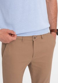 Pull en tricot bleu clair associé à un pantalon beige. Le pantalon a une texture lisse et une fermeture à boutons avec une fermeture éclair cachée.