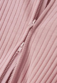 Mjukt rosa ribbat tyg, med en slät dragkedja med dubbla dragflikar. Texturen är fin och jämn genom hela materialet.