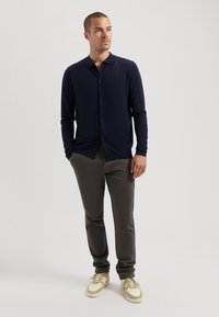 Tengerészeti hosszú ujjú gombos ing, szürke slim-fit nadrággal és bézs sportcipővel párosítva. Sima textúra, testre szabott dizájn, egyszerű gombos részletezés.
