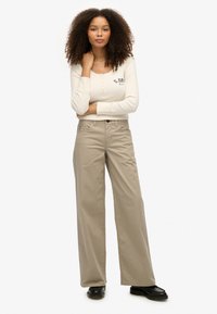 Beige wijde broek van katoen, met een knoopsluiting en zijzakken. Gecombineerd met een crèmekleurige blouse met lange mouwen en knopen.