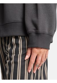 Węgorzowy sweter z prążkowanymi mankietami, o luźnym kroju. W połączeniu z czarnymi spodniami, pionowe beżowe paski tworzą kontrastującą teksturę.