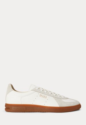 Weißer Sneaker mit niedrigem Schaft, beigen Wildlederakzenten, brauner Gummisohle, weißen Schnürsenkeln und kleinem Polo-Logo an der Seite.