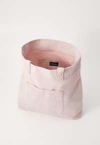 Sac en velours côtelé rose avec une texture douce, ouvert sur le dessus, et une petite poche extérieure dotée d'accents en métal doré. L'intérieur est également doublé de rose.