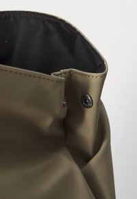 Gros plan sur une botte de pluie vert olive avec une doublure intérieure noire et un bouton-pression métallique près du bord supérieur.