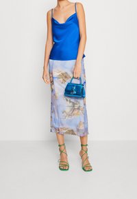 Blå satin camisole med tunna band, blommönstrad genomskinlig midikjol i pastellfärger och en glänsande blå handväska. Gröna sandaler med remmar.