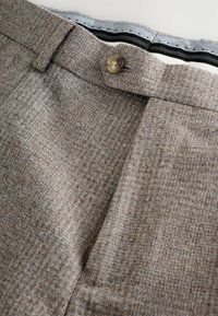 Braune karierte Hose aus strukturiertem Stoff. Mit einem Knopfverschluss und einem kontrastierenden Innenbund mit Hahnentritt-Muster.