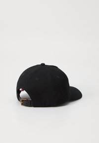 Black cap with a curved brim, fabric texture, adjustable leather strap at the back, and a small red, white, and blue accent tag.