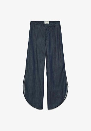 Tamne traper hlače širokih nogavica s zaobljenim prorezima na rubu s obje strane, prednji patentni zatvarač i oznaka na pojasu s natpisom AWARE.