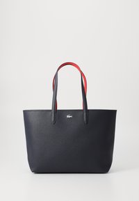 Tote en cuir grainé bleu marine avec des poignées rouges contrastées, présentant un design minimaliste et un petit logo au centre à l'avant.