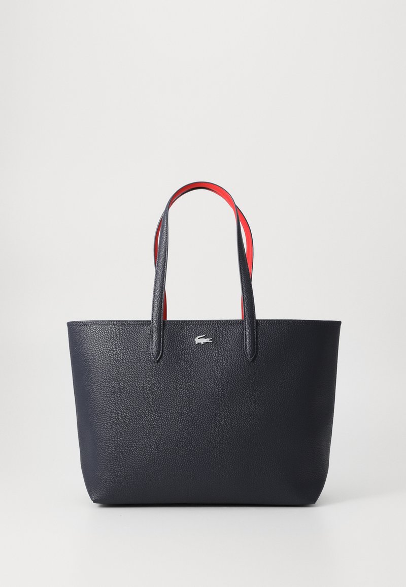 Bolsa tote de pele texturizada azul-marinho com alças vermelhas em contraste, apresentando um design minimalista e um pequeno logotipo no centro da parte frontal.