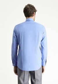 Camicia azzurro chiaro a maniche lunghe con polsini abbottonati. Tessuto morbido, vestibilità sartoriale, orlo curvo e dettagli sulla spalla.
