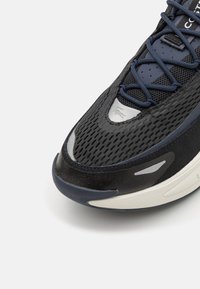 Baskets de sport noires et bleues avec une tige en mesh, un col rembourré et une semelle en caoutchouc. Des accents argentés notables rehaussent les détails de conception.