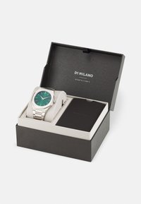 Silver stainless steel watch with a green dial and silver markers, presented in a black box with a white cushion and black booklet inside.
