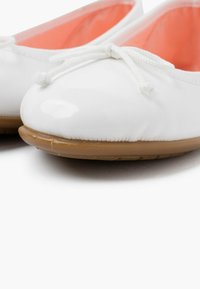 Ballerine in pelle verniciata bianca con punta rotonda, caratterizzate da un sottile fiocco in pizzo bianco e una suola in gomma color cammello. Interno evidenziato in corallo.