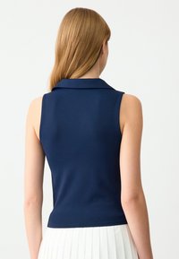 Polo top senza maniche di colore navy con colletto, design aderente e texture liscia. Presenta una silhouette pulita, abbinata a una gonna bianca plissè.
