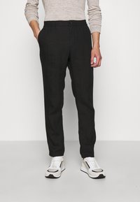 Černé lněné kalhoty s elastickým pasem a zapínáním na knoflík, v kombinaci s bílými a černými teniskami. Hladká textura, přiléhavý střih.