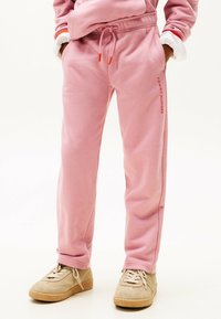 Roze katoenen sweatpants met een elastische tailleband, zijzakken en het 'TOMMY HILFIGER' logo in het rood, gecombineerd met beige sneakers.