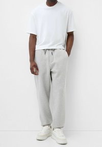 Weisses Baumwoll-T-Shirt, lockere Passform, kombiniert mit hellgrauen Jogginghosen mit elastischem Bund und schmal zulaufenden Bündchen. Sneaker runden den Look ab.