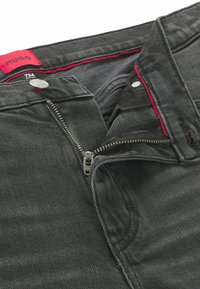 Jeans in denim nero con zip, caratterizzati da una zip argentata, un'etichetta rossa e dettagli all'interno della vita. Inquadratura ravvicinata dell'apertura frontale.