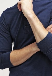 Námorně modrá polokošile s dlouhým rukávem a límečkem, vybavená légou s knoflíky a kontrastními manžetami. Měkká, strukturovaná tkanina.