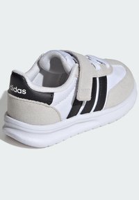 Biele tenisky so semišovými šedými akcentmi, čiernymi pruhmi a suchým zipsom. Obsahujú textúrovanú podrážku a polstrovaný interiér pre pohodlie.