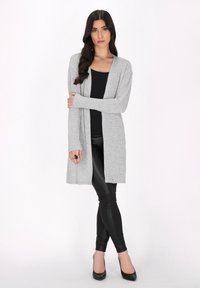 Grauer langer Cardigan aus weichem Stoff, offenes Design ohne Knöpfe, kombiniert mit schwarzen Leggings und Schuhen. Glatte Textur, vielseitiger Stil.