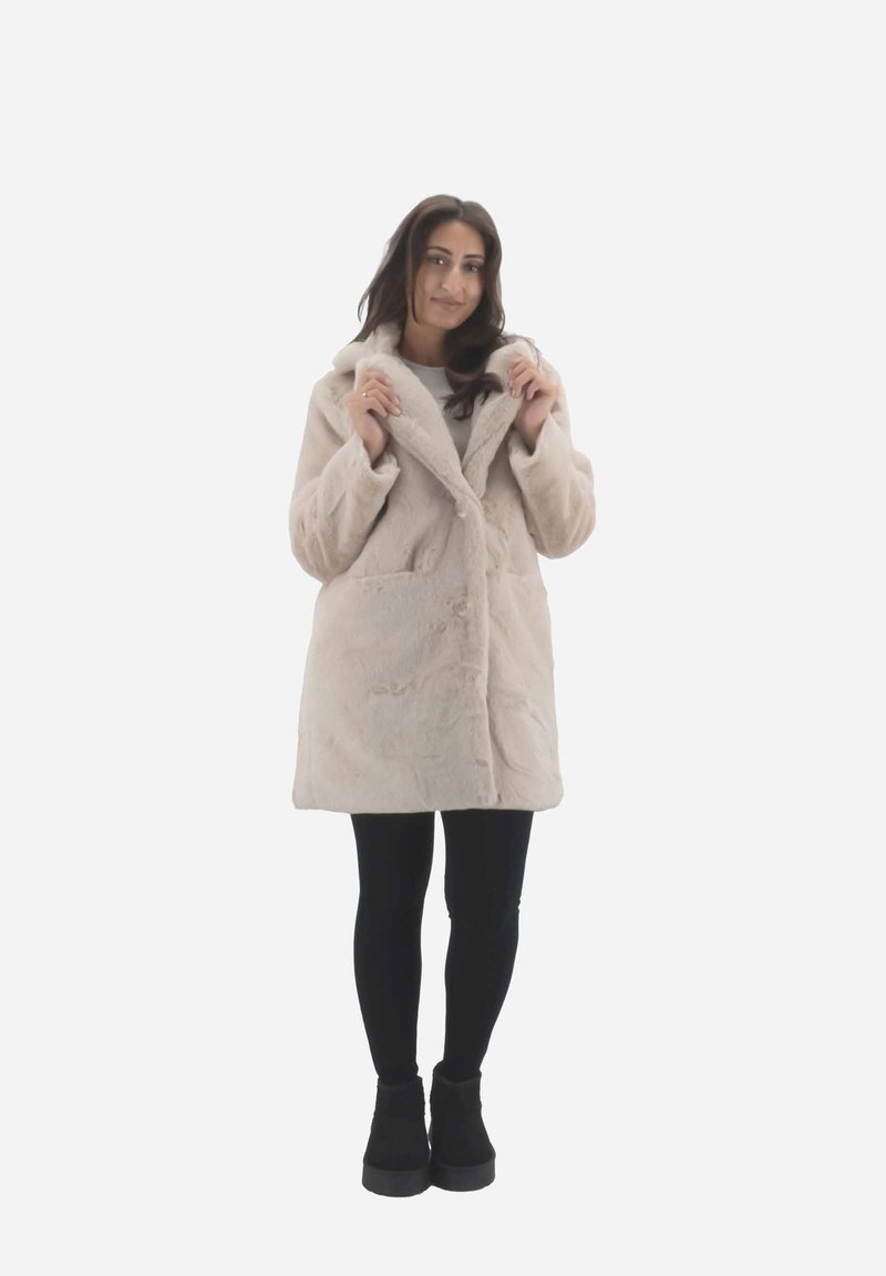Beige faux fur frakke med en afslappet pasform, stor krave og frontknapper. To sidelommer, parret med sorte leggings og ankelstøvler.