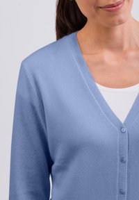 Ljusblå cardigan med V-ringning, långa ärmar och tre knappar framtill. Mjuk textur med en slät yta.