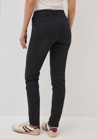 Jeans negros ajustados de cintura alta, con dos bolsillos traseros y un diseño ceñido. Combinados con zapatillas deportivas beige que tienen acentos burdeos.